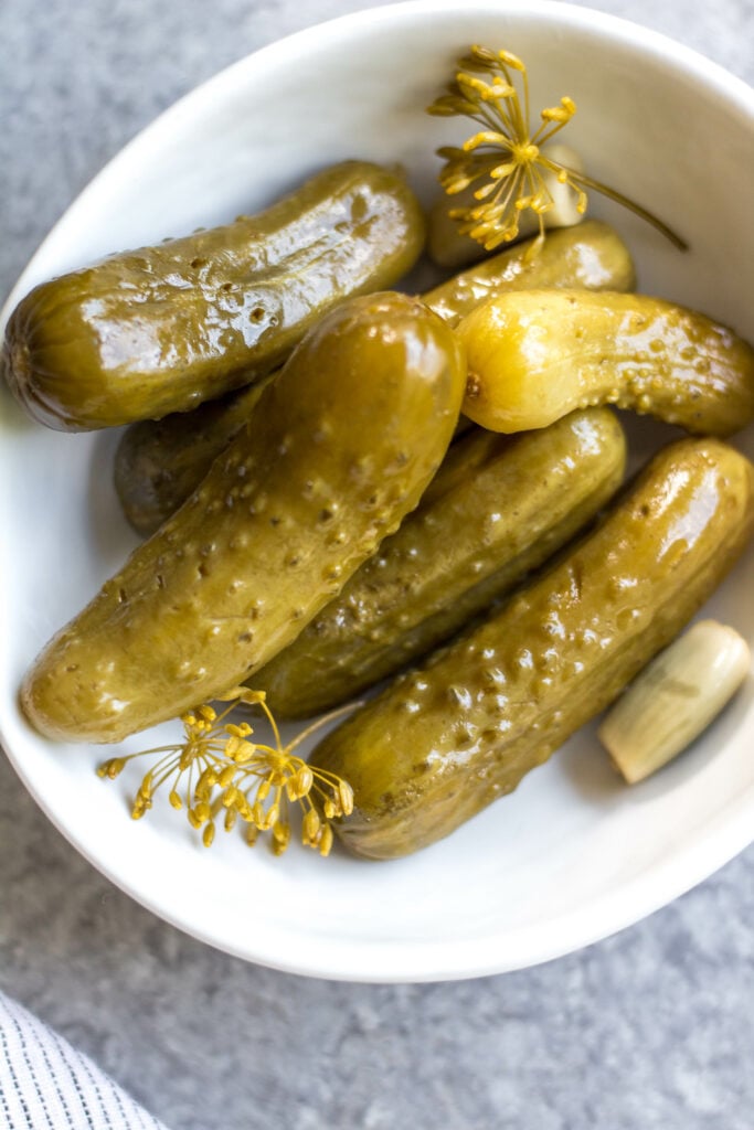 This recipe for canned pickles has been in my family for over 100 years. It's easy, even for a canning beginner, only requires 7 ingredients, including garlic, dill and onions to give them their classic flavor. The mini cucumbers can be crinkle cut into slices, cut into spears, or left whole. This homemade dill pickle recipe yields 40 jars, so you can enjoy them all year, share with family and give as gifts! #homemadepickles #dillpickles #picklerecipe #picklebrine